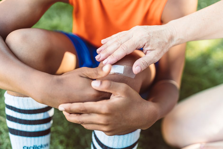 pexels-photo-8798943-12 A close-up view of an adult applying a band aid to a child's wounded knee outdoors during the day.